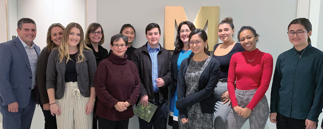 A group of people stand in a room in front of a large "M" logo